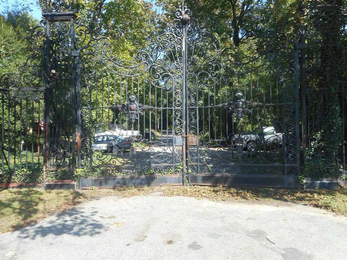 Tall iron gates between stone piers under trees