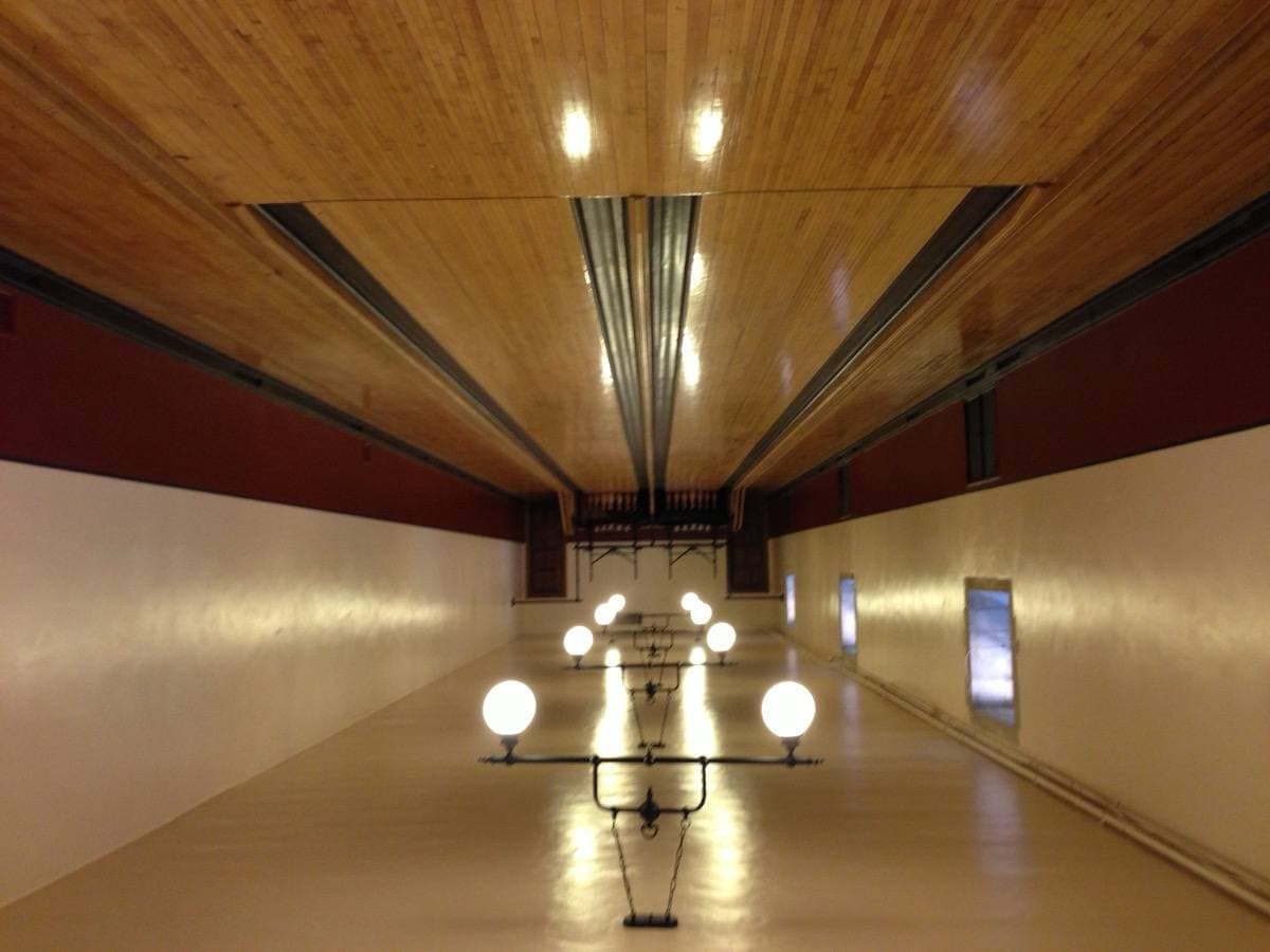 A long wooden two-lane bowling alley under hanging globe lights, pins at the far end