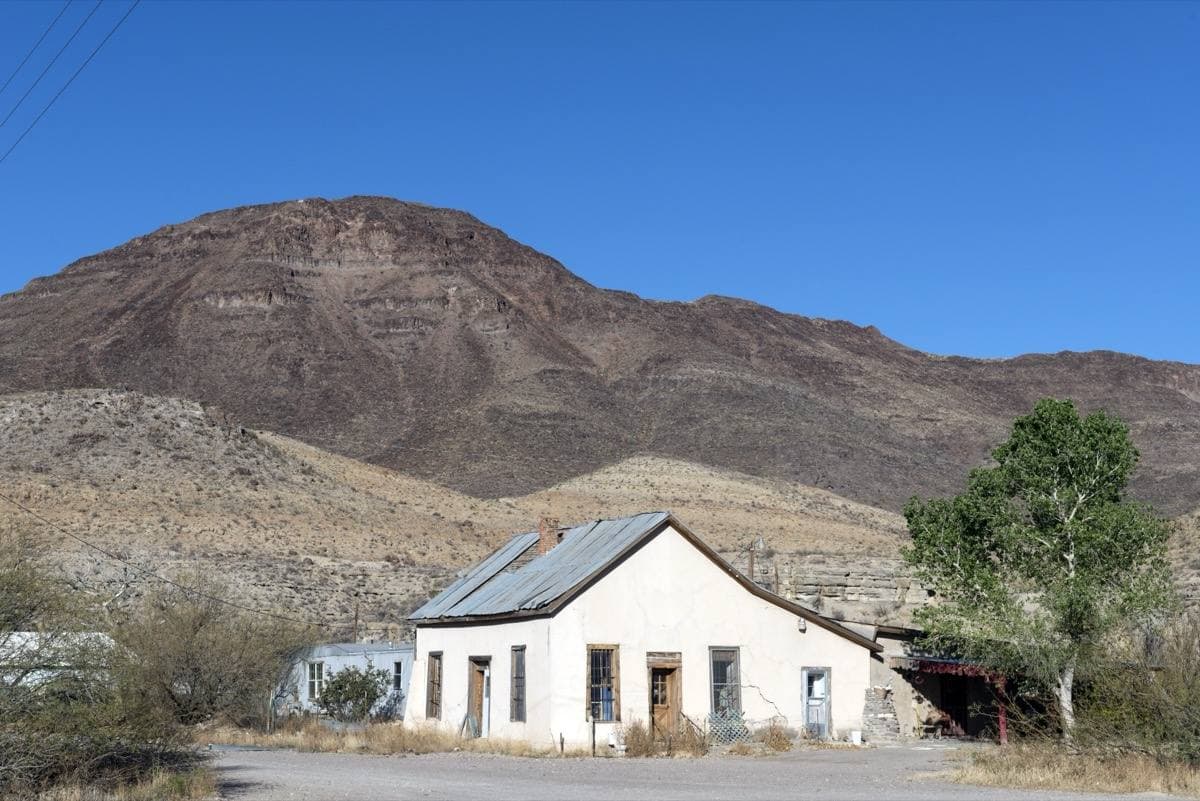 A small white church with a tin roof below a bare brown mountain