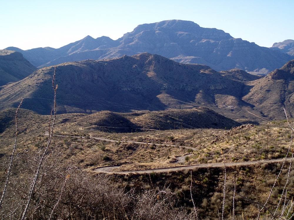 A gravel road running through dry grassland toward low mountains