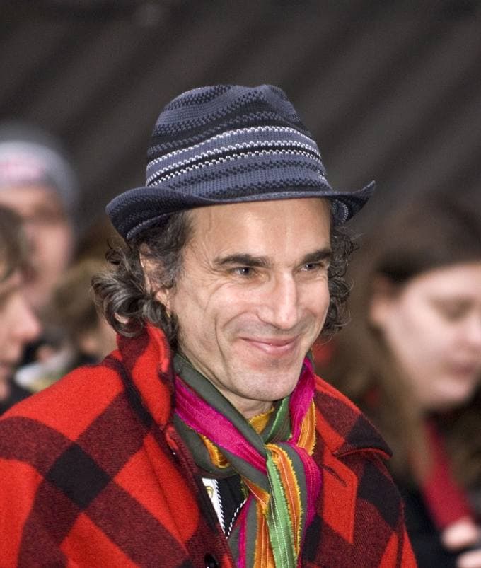 Daniel Day-Lewis smiling in a knitted hat, a bright scarf and a red plaid coat, a crowd behind him