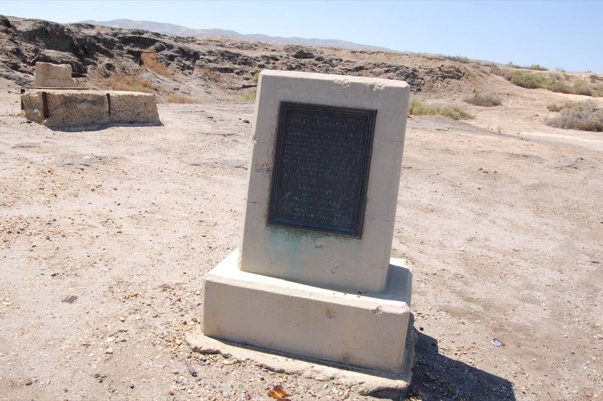 A bronze plaque on a stone plinth in bare desert ground