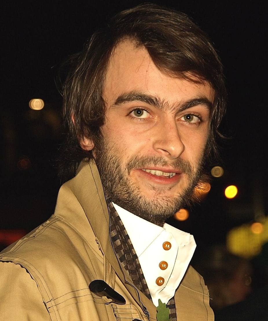 Joe Gilgun in a camel duffel coat with a poppy, at night