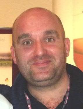Shane Meadows, shaven-headed, smiling, in a dark top with a festival lanyard