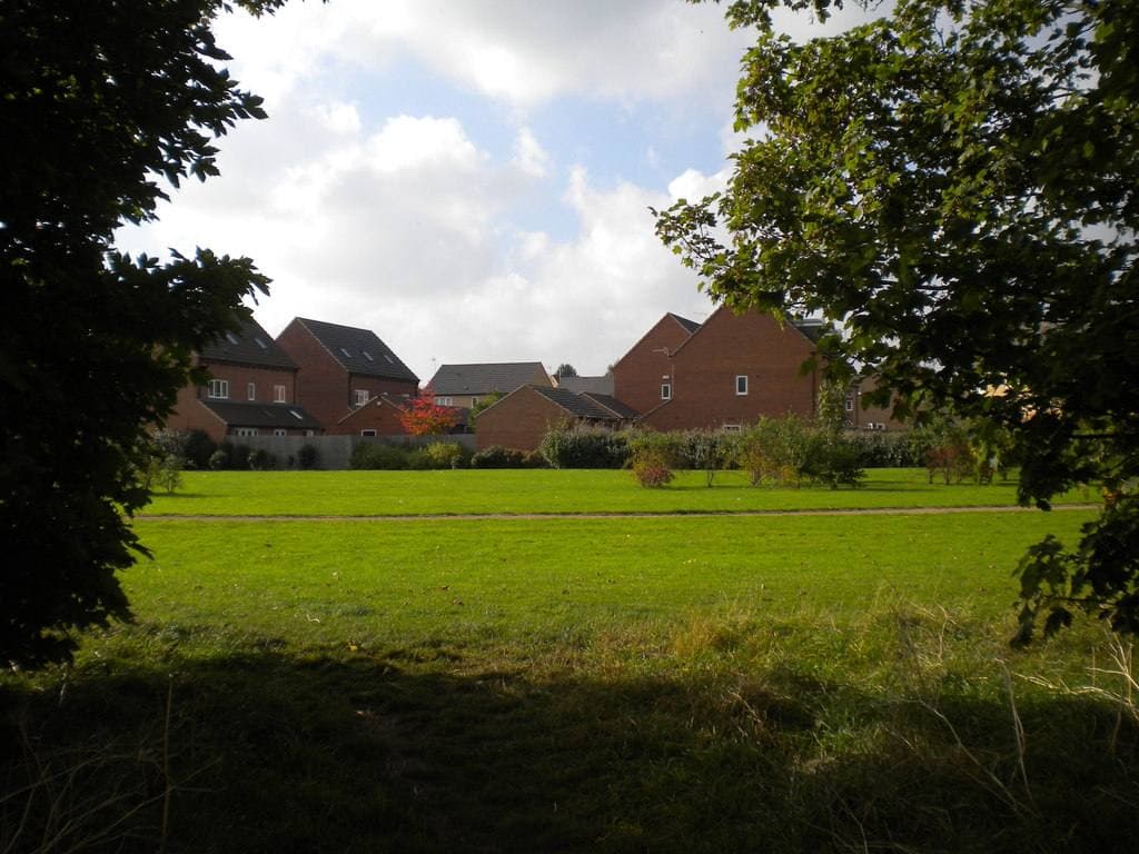 New brick houses beyond a green, framed by trees