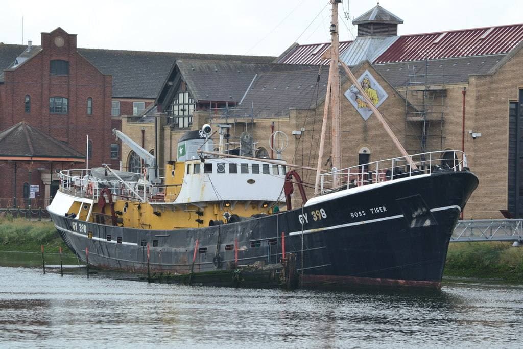 A black-hulled trawler moored in front of brick dock buildings