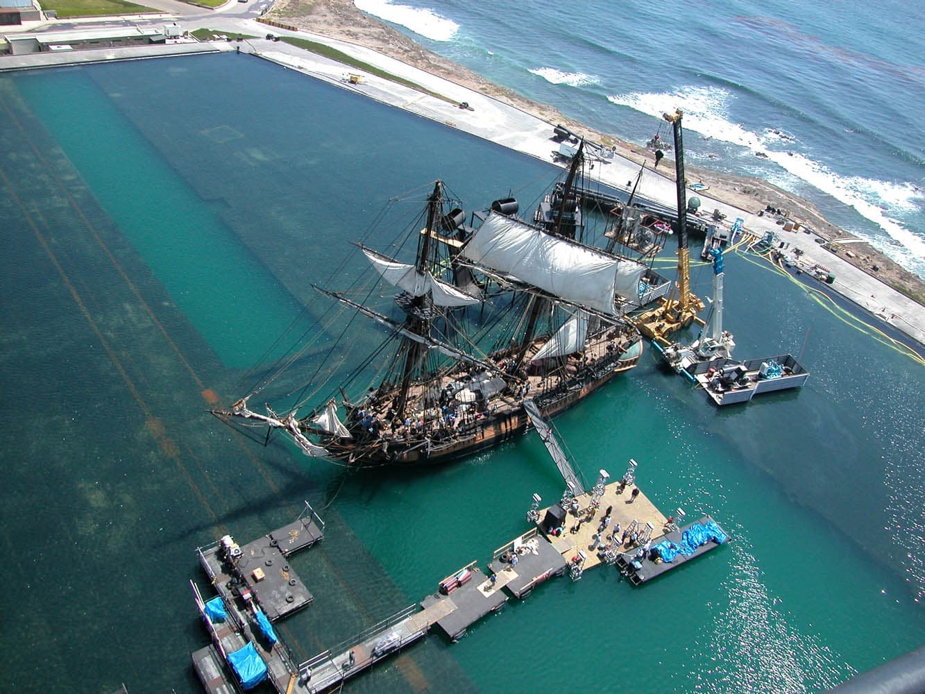 An aerial view of a huge seawater tank beside the Pacific with a sailing ship in it