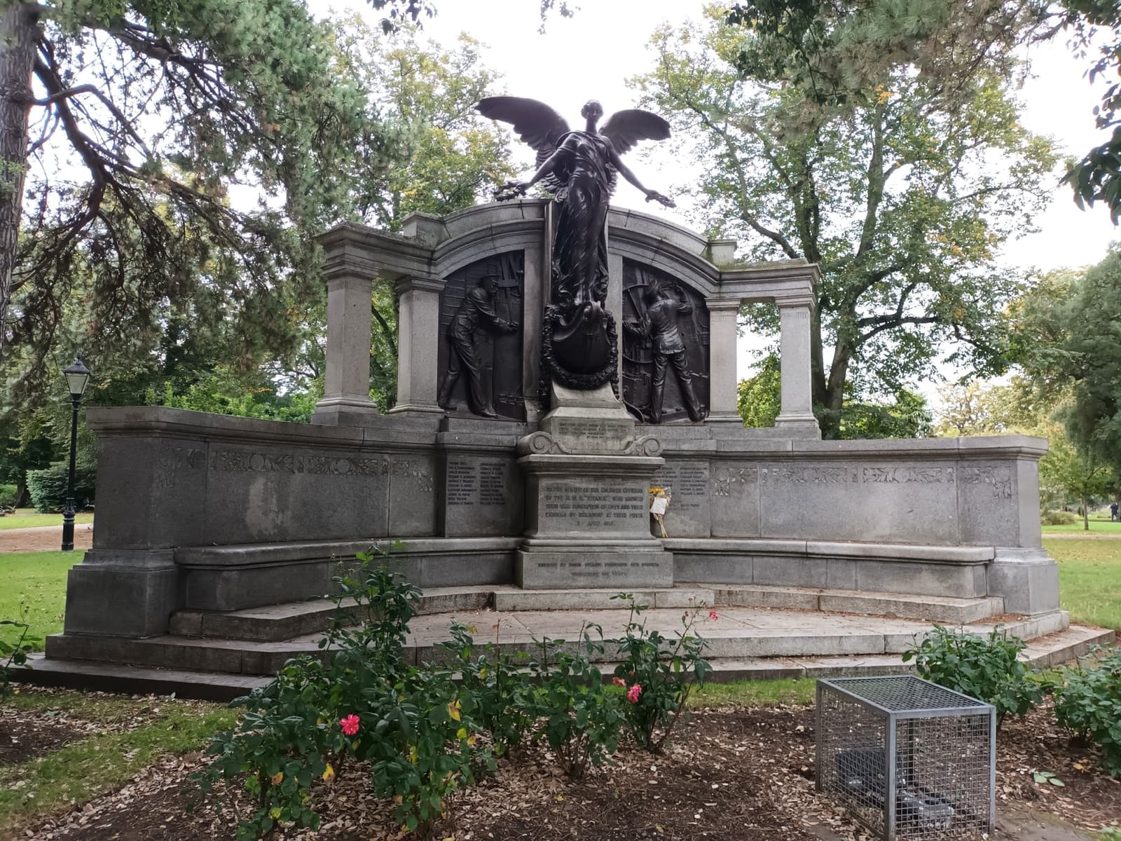 A granite memorial with bronze figures and a winged statue among trees