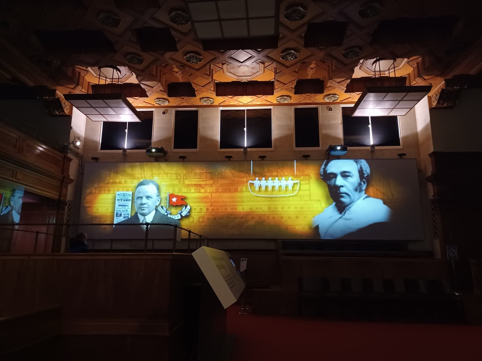 A dark gallery with faces of crew projected on a wall