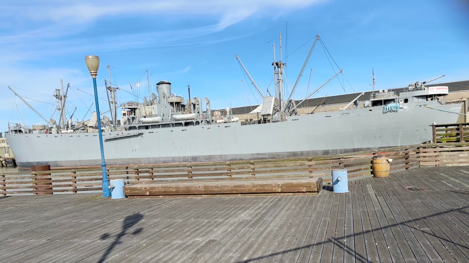 A grey Liberty ship moored along a wooden pier
