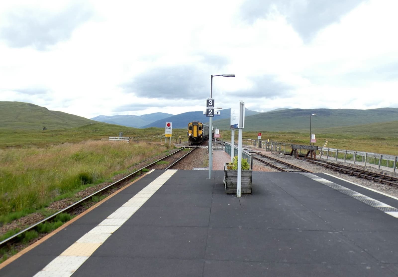 A long empty platform on open moor with a small train in the distance and hills behind