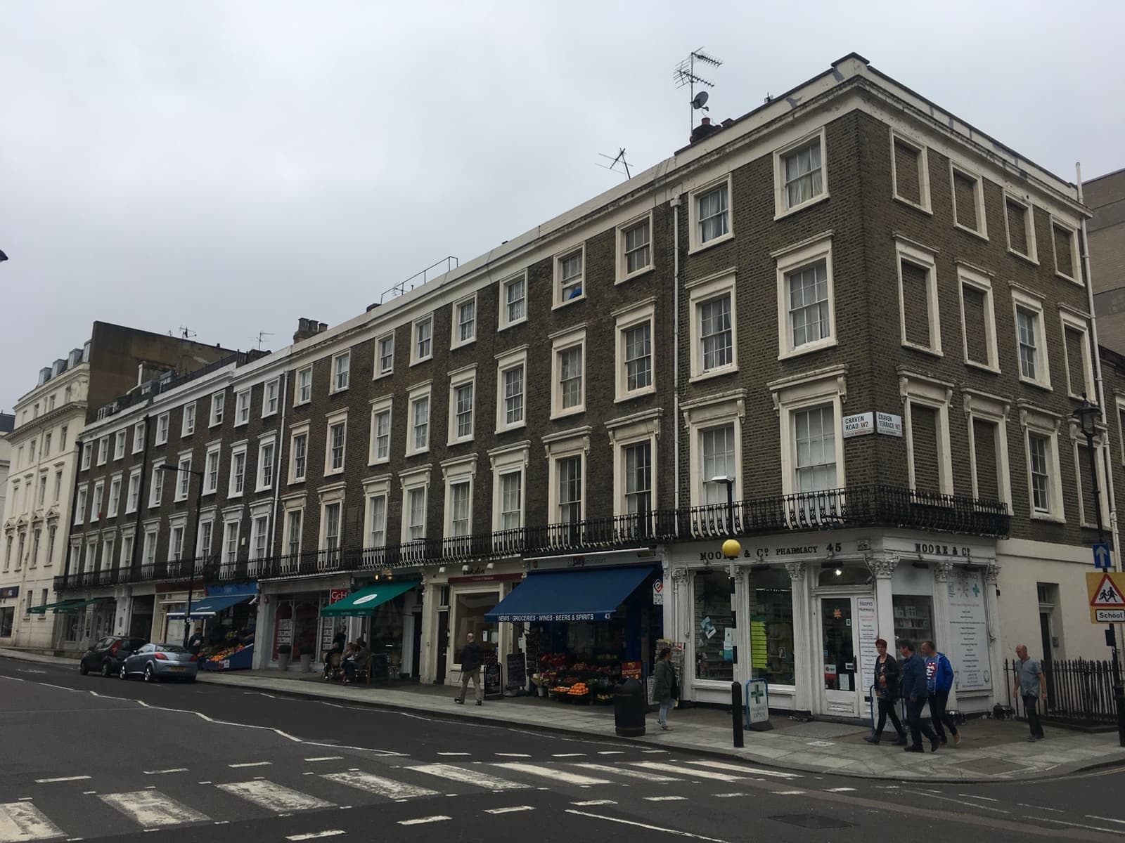 A long cream and brick terrace with shops on the ground floor on a London corner