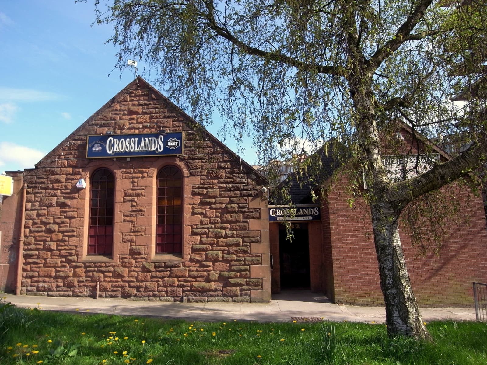 A red sandstone pub with a gabled front and a Crosslands sign, behind a birch tree