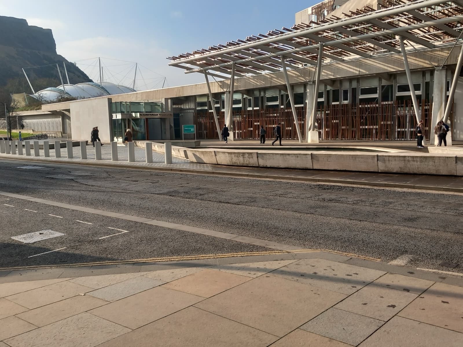 A modern parliament entrance with a steel canopy, crags rising behind