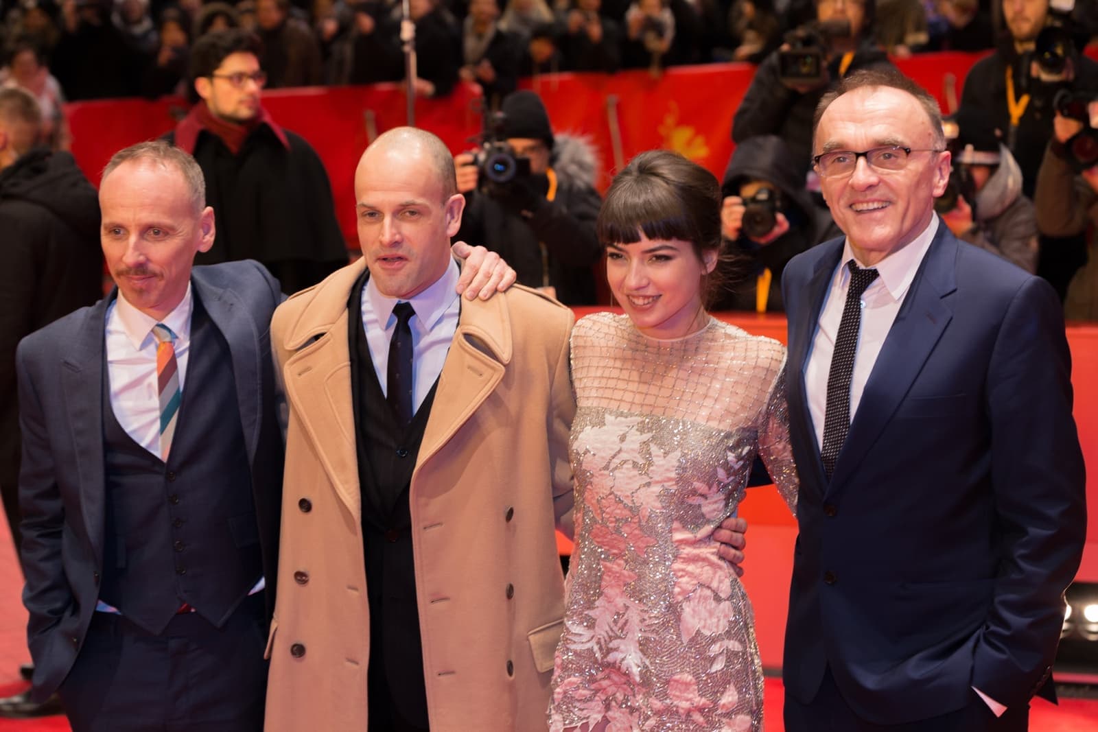 Four people on a red carpet in front of photographers