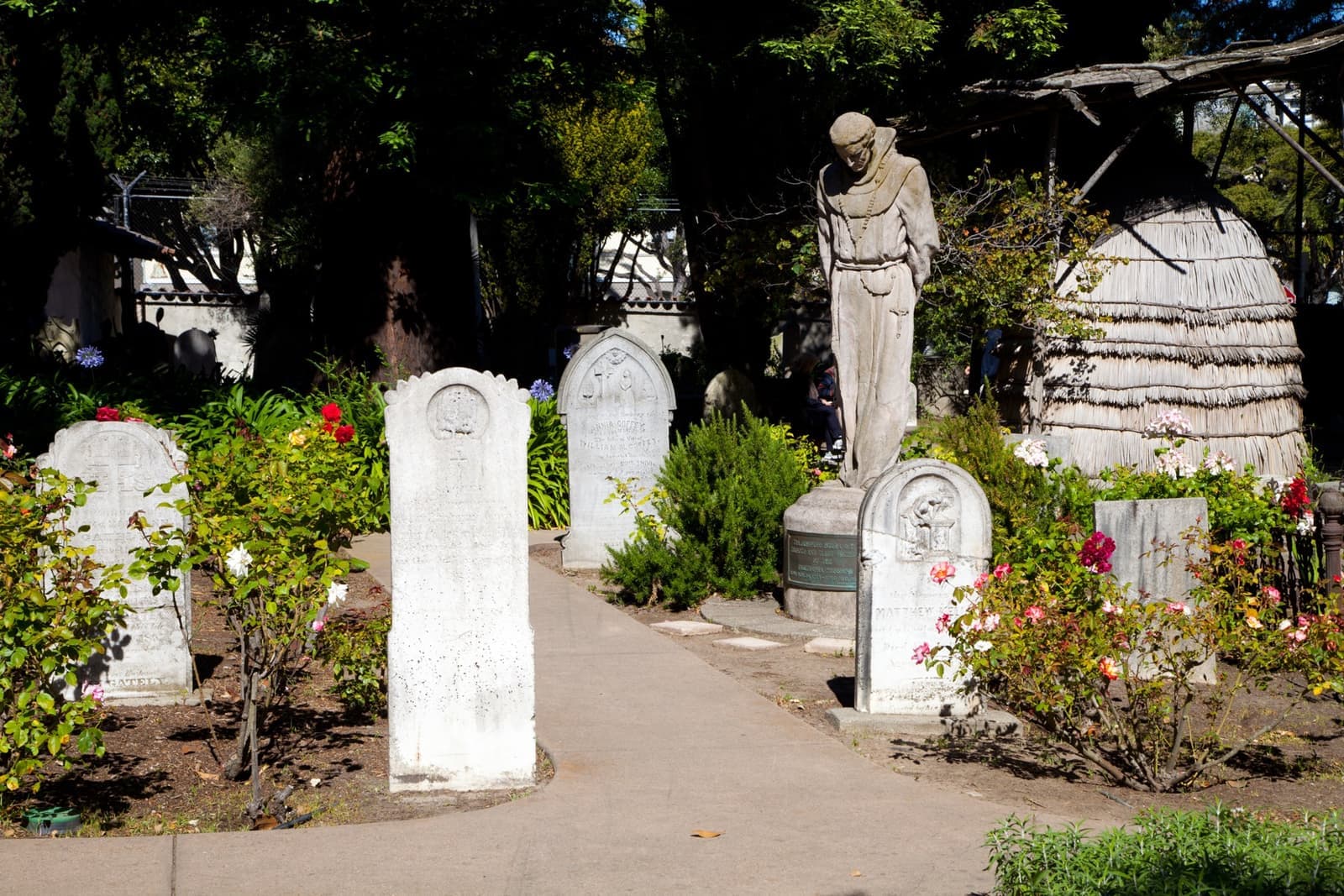 A cemetery path with white headstones, roses and a cloaked statue