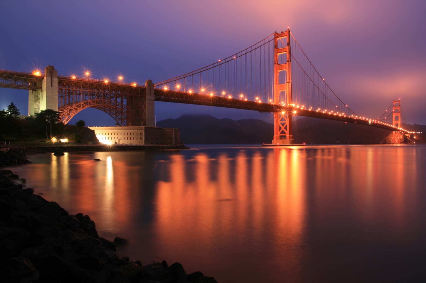 A brick fort lit at dusk beneath the illuminated bridge