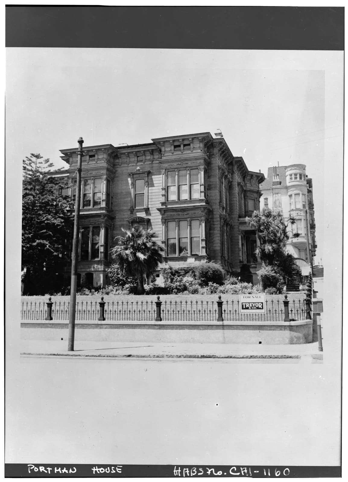 A Victorian mansion behind an iron fence and palms