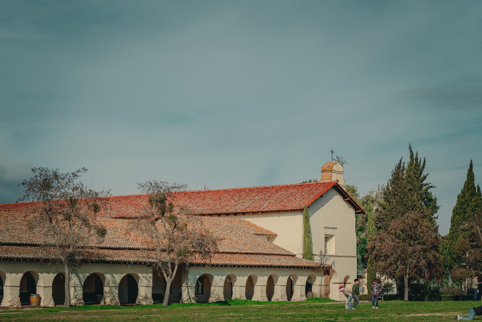 A mission church and arcade with a tiled roof across a lawn