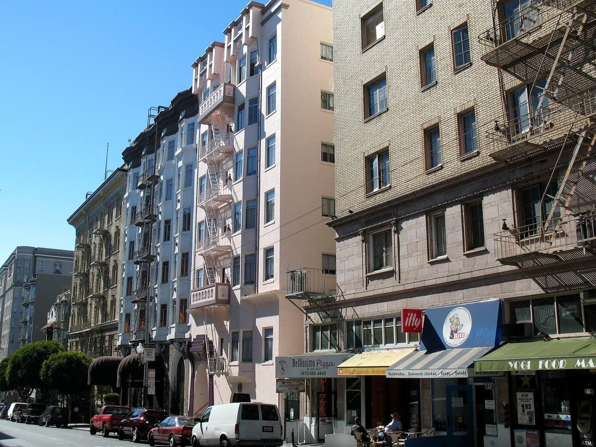 Tall apartment hotels with fire escapes along a sunny street