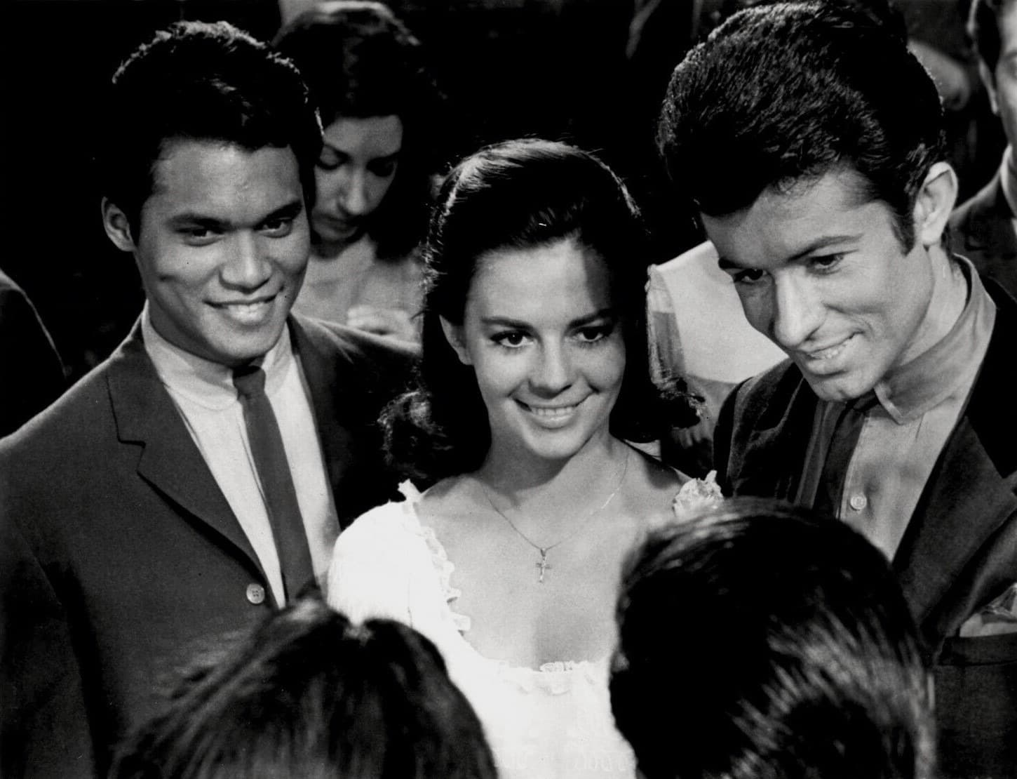 Natalie Wood in a white dress smiling, between two young men in dark suits