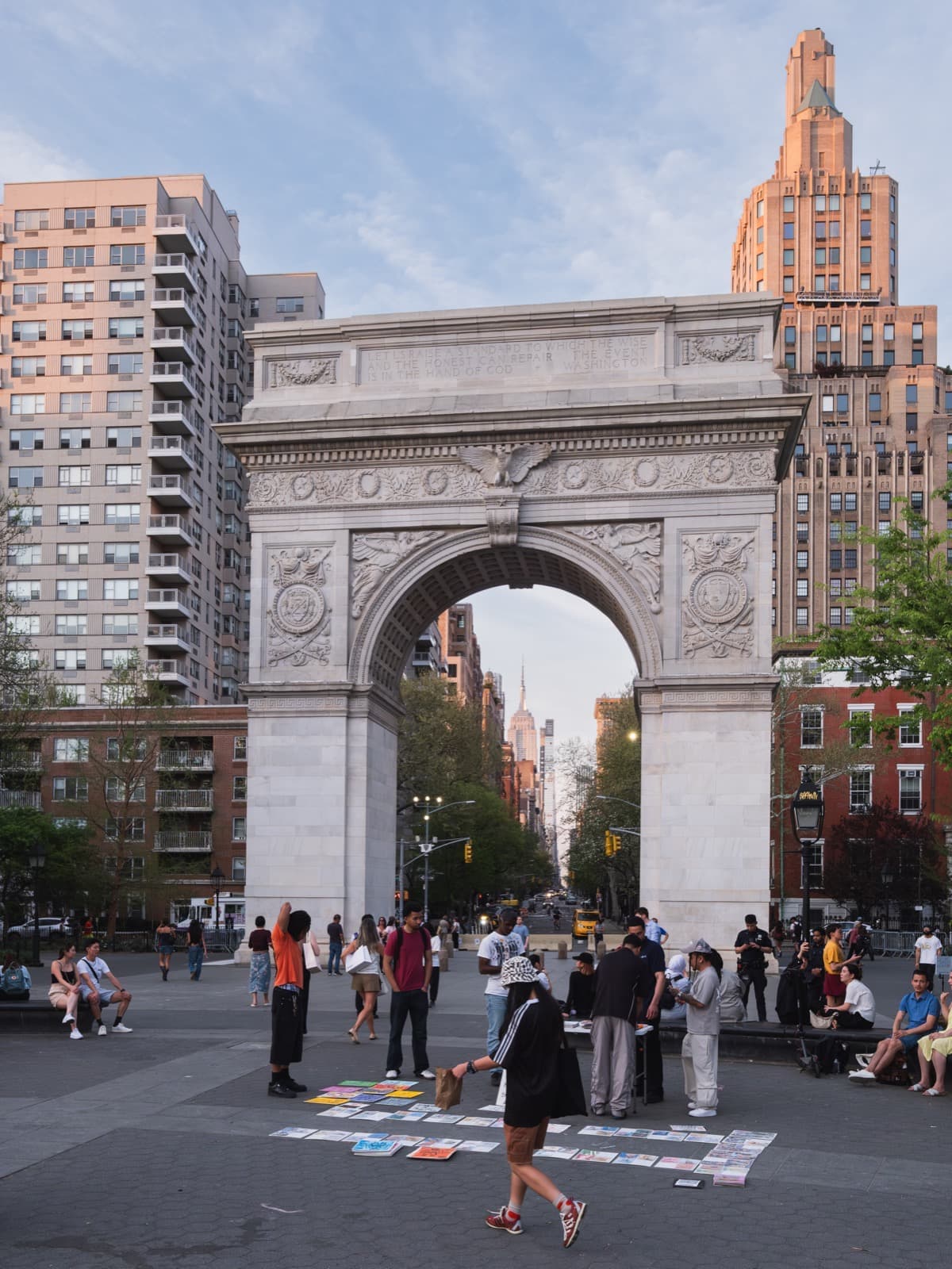 A white marble triumphal arch at the edge of a busy square, a tower visible through it