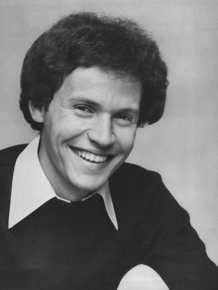 A young Billy Crystal with curly hair, laughing, in a black-and-white portrait