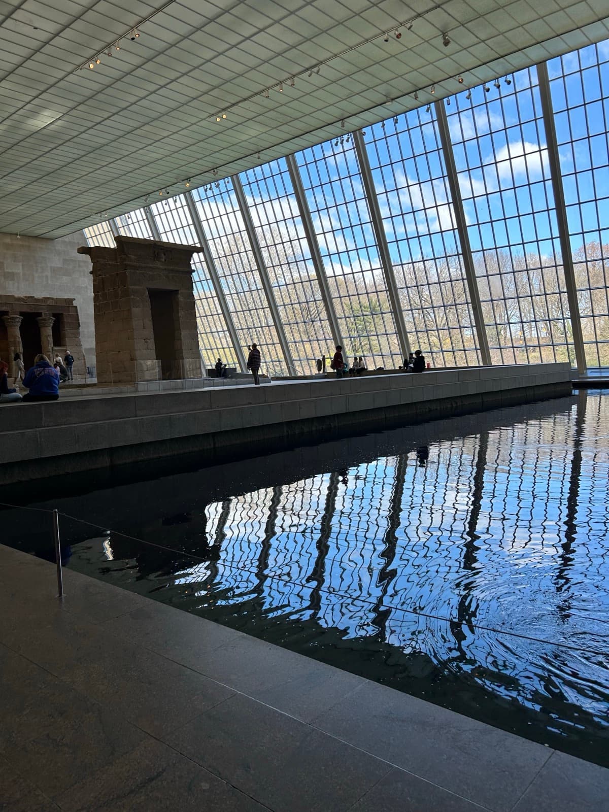 A long pool in a glass-walled gallery, trees outside the slanted windows