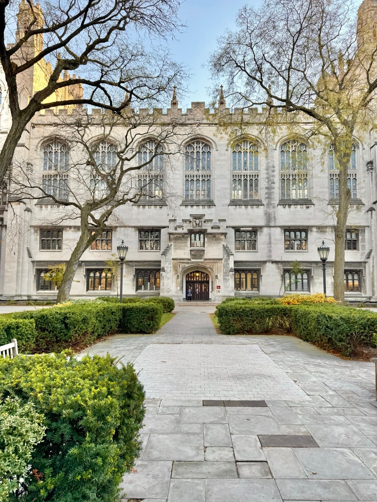 A Gothic stone library front with twin towers behind autumn trees on a lawn