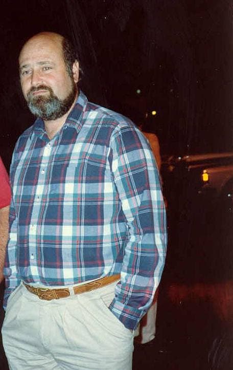 Rob Reiner, bearded, in a checked shirt and pale trousers, at night