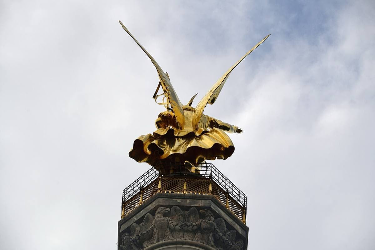 A gilded winged figure on top of a column against a pale sky