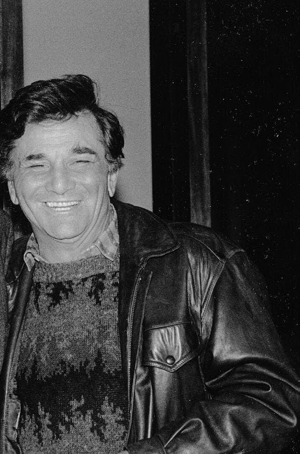 Peter Falk in a leather jacket and patterned jumper, smiling, black-and-white