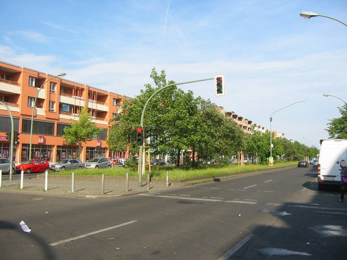 A wide street with apartment blocks, trees and parked cars