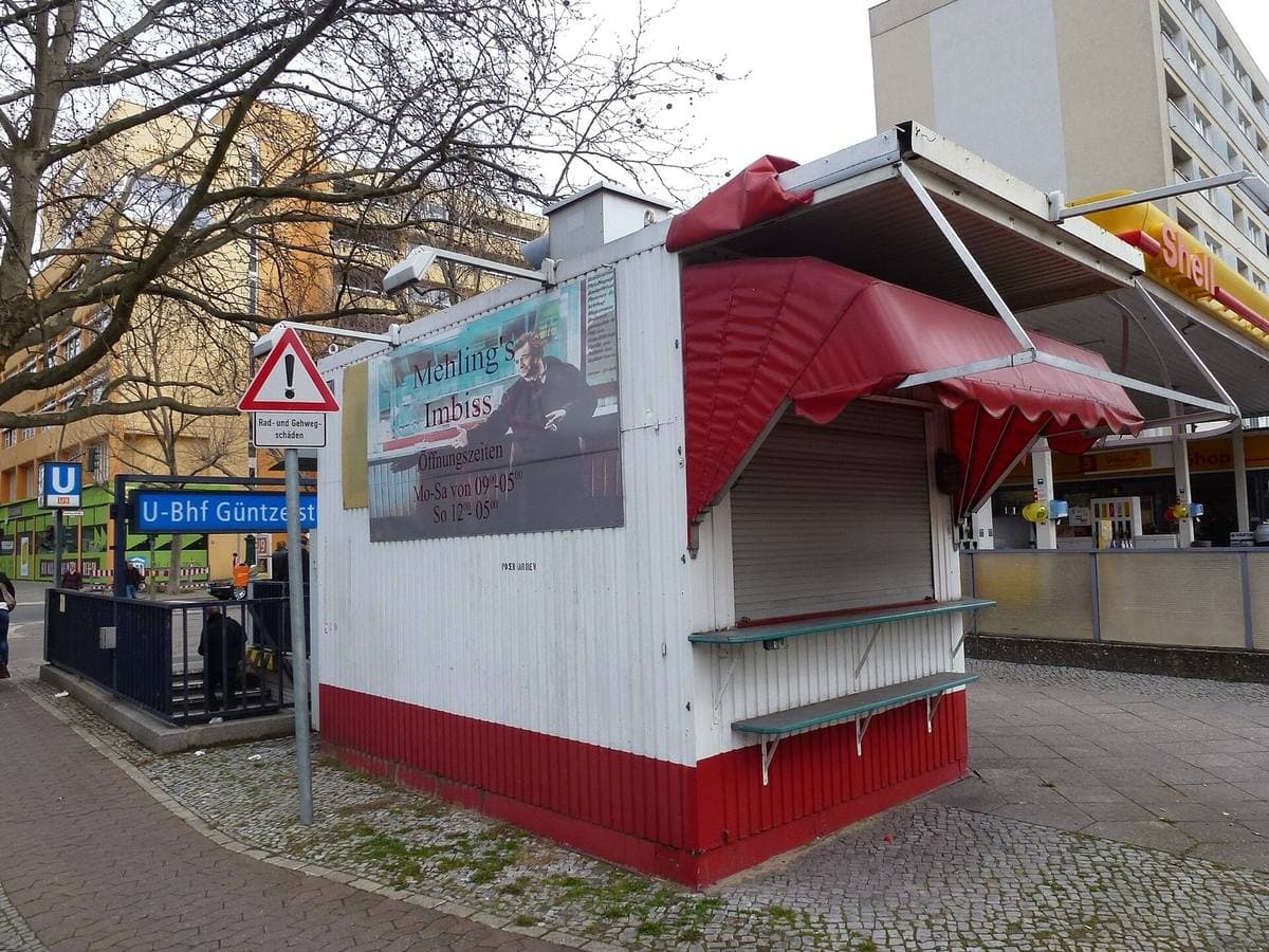 A closed white-and-red kiosk with a canopy on a pavement corner