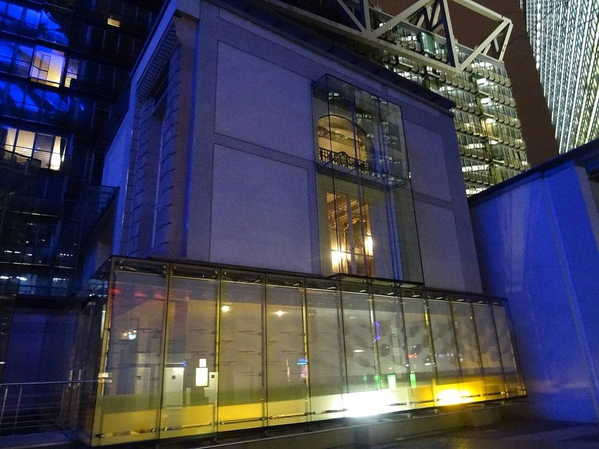 An old hotel façade inside a glass atrium, lit blue at night