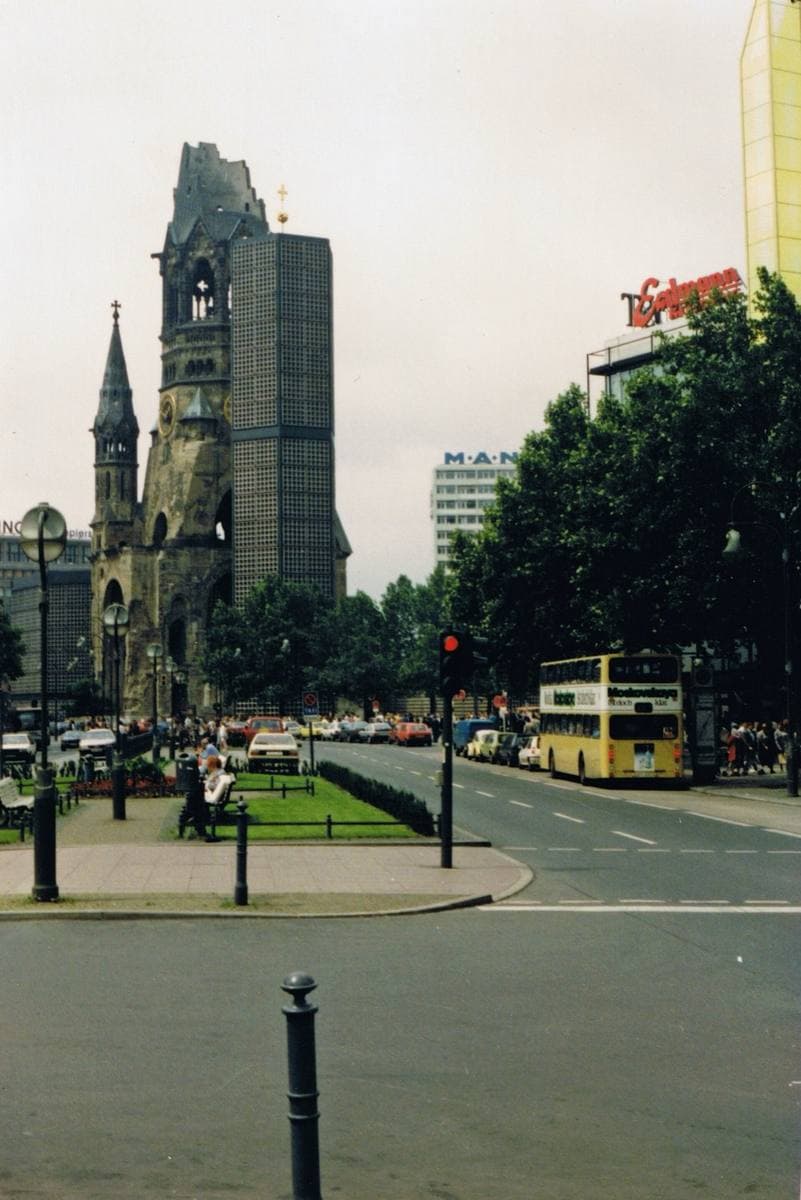 The broken church spire beside a modern tower, with traffic and a double-decker bus