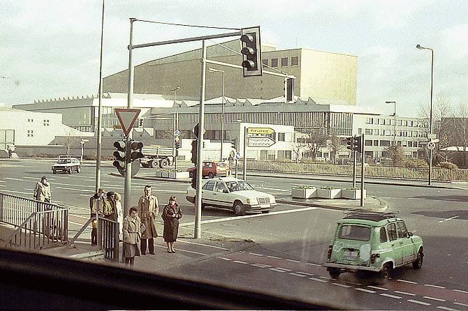 A long pale library building behind a road junction, with cars and a traffic light