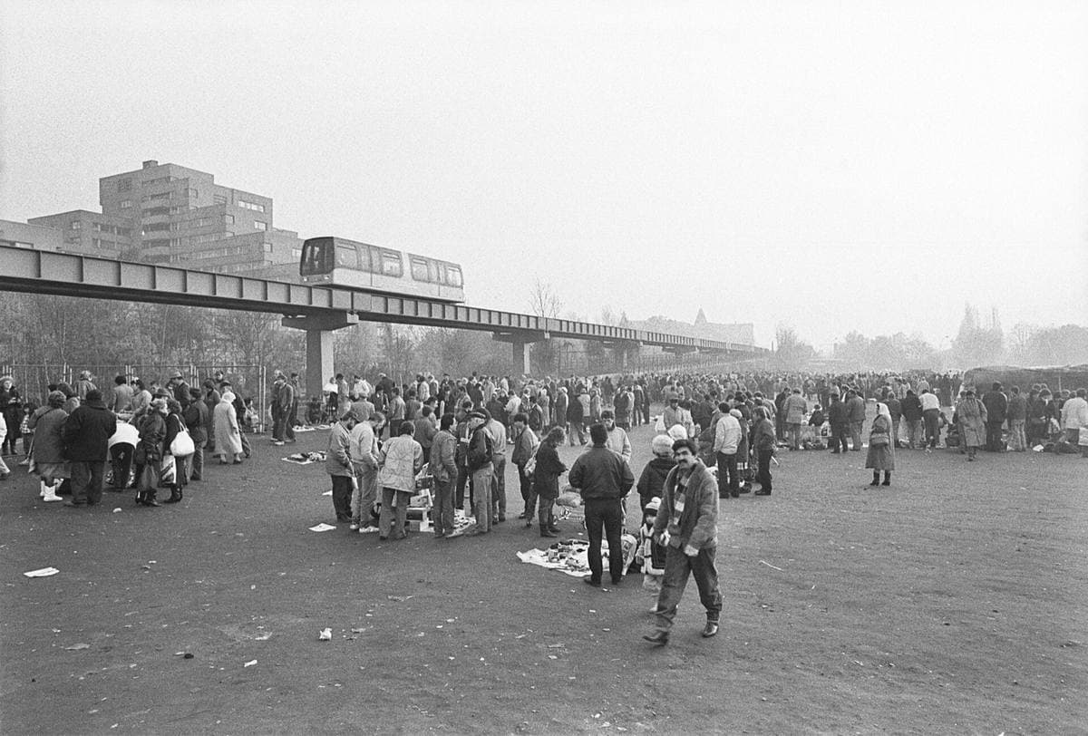 Crowds at an open-air market with an elevated track running behind, black-and-white