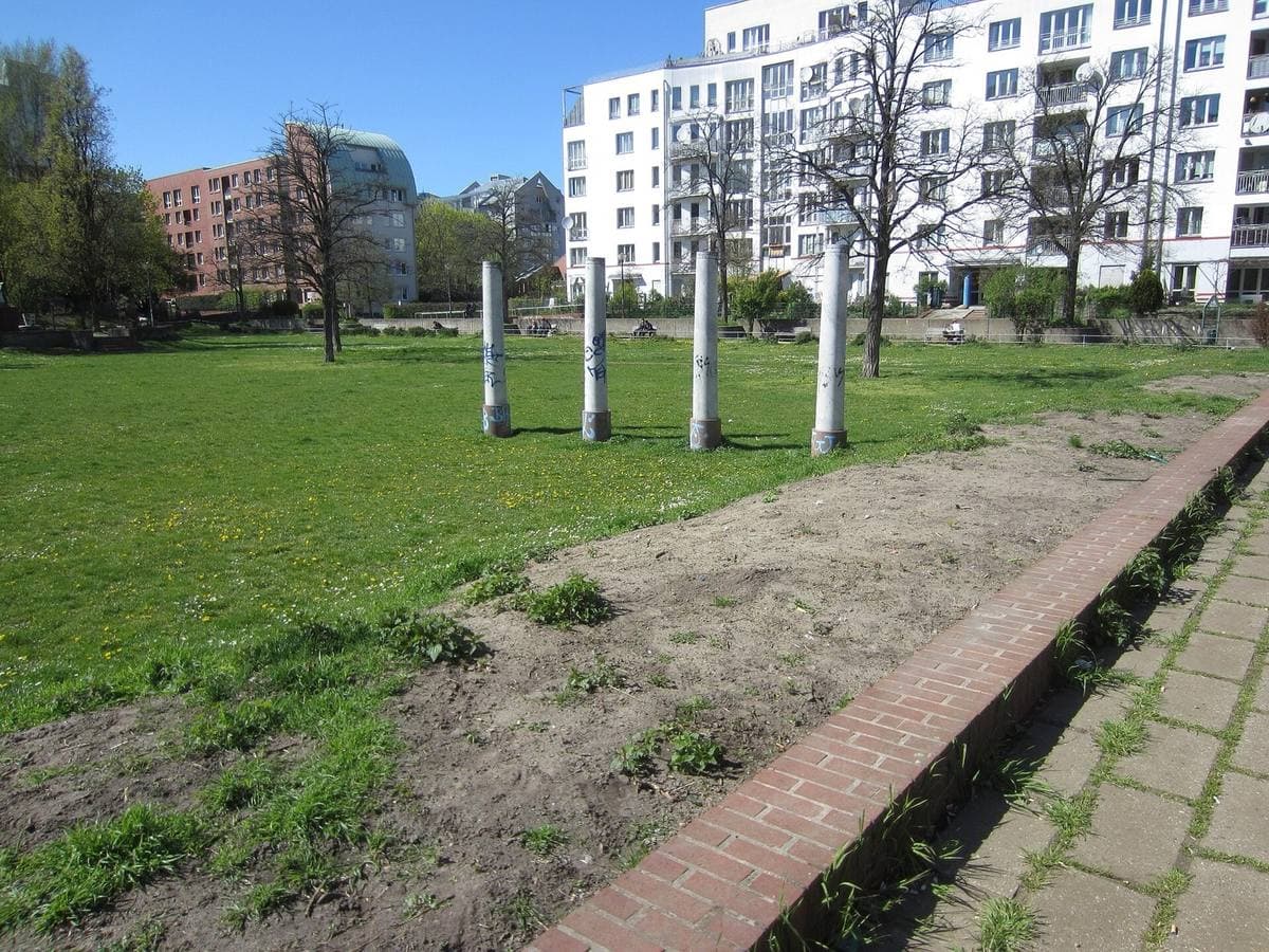 A grassy park with tall white posts and apartment blocks behind