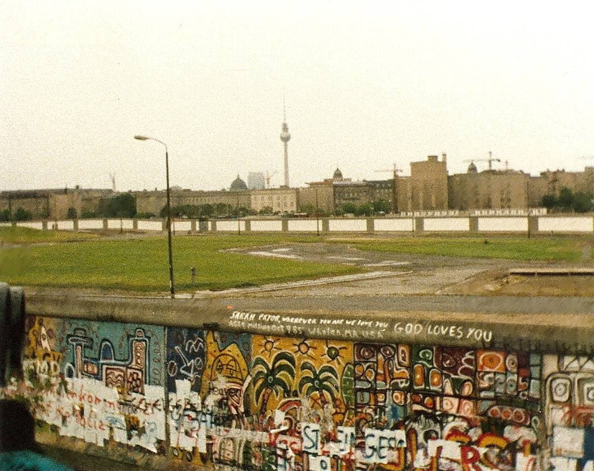 A painted wall across rough ground, with the Berlin television tower in the distance