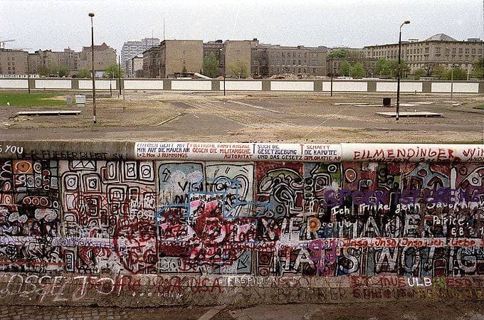 Graffiti on the Berlin Wall in front of an empty strip and distant buildings