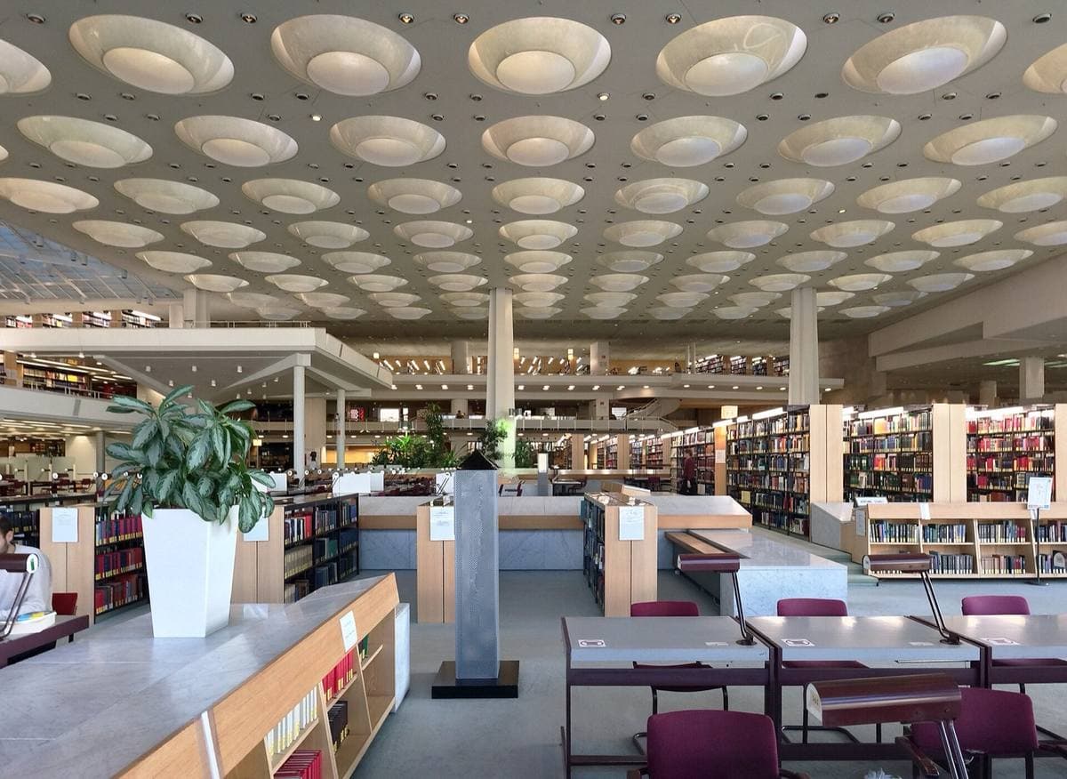 A wide reading room with rows of desks under a ceiling of round skylights
