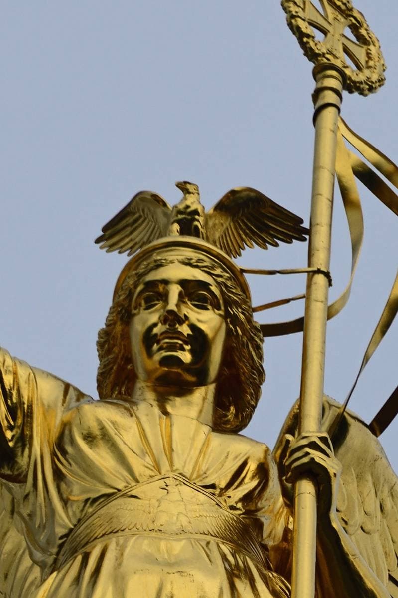 Close view of a gilded statue with a laurel wreath and a staff