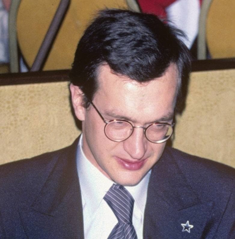 Wim Wenders in round glasses and a striped tie, looking down