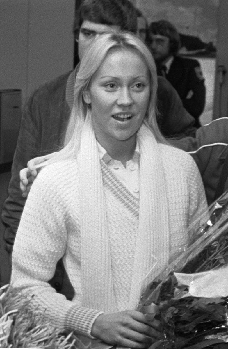 Agnetha Fältskog in a white knitted jumper and scarf, holding flowers