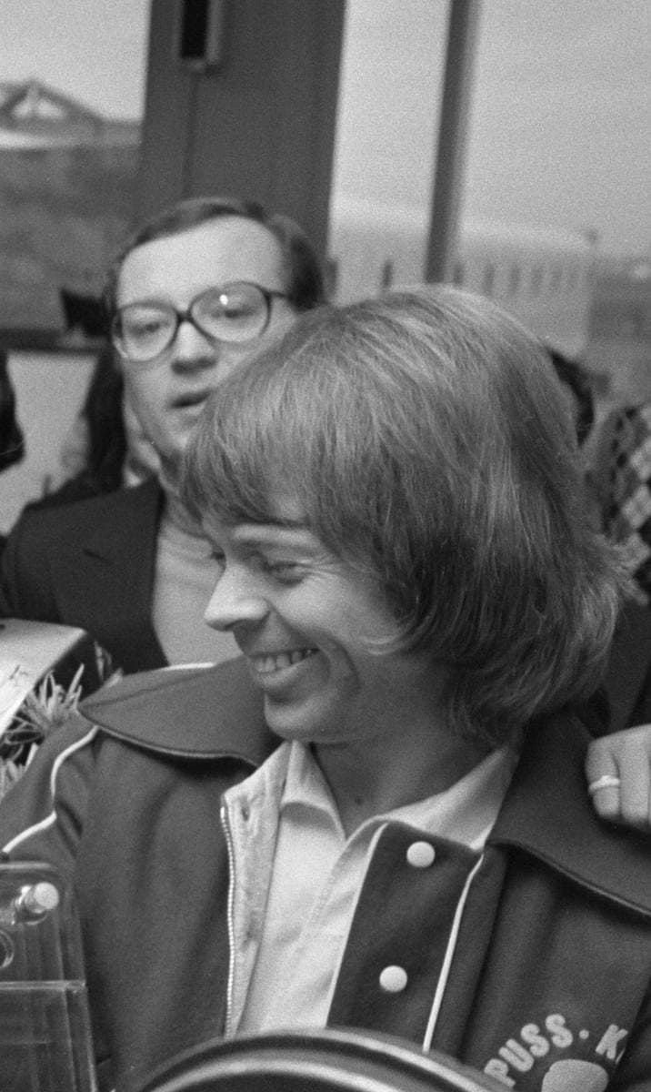 Björn Ulvaeus with a fringe, smiling, in a jacket in an airport crowd