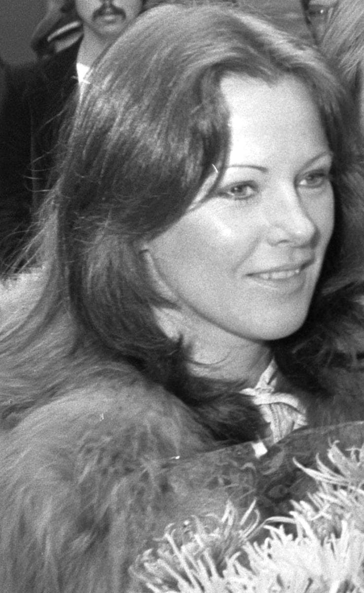 Anni-Frid Lyngstad smiling, in a fur collar, flowers in front of her