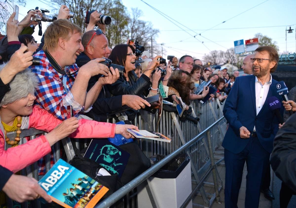 Björn Ulvaeus in a blue suit beside a crowd of fans holding cameras and ABBA books behind a barrier