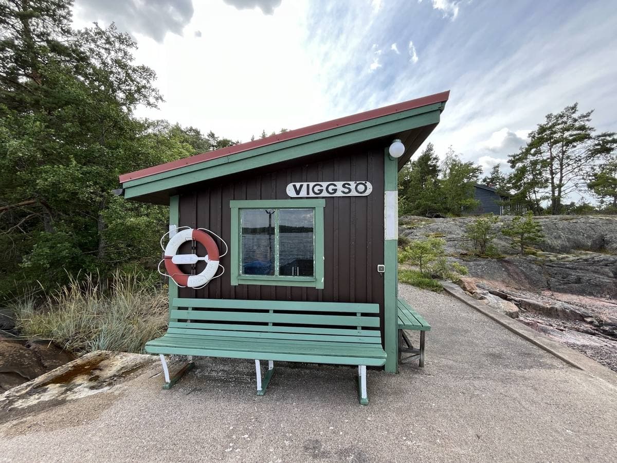 A small green and brown waiting shelter with a lifebuoy on the rocks by the jetty