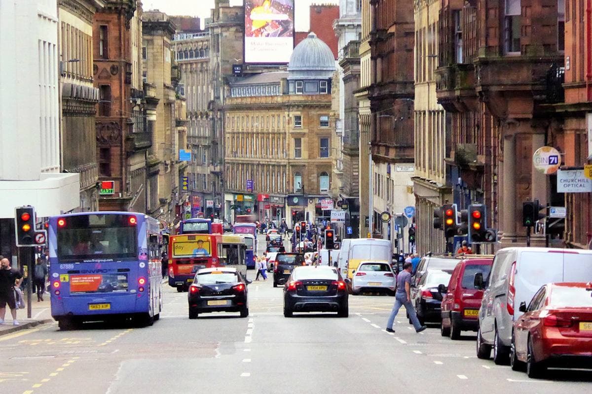 A busy city street of sandstone buildings with buses and cars